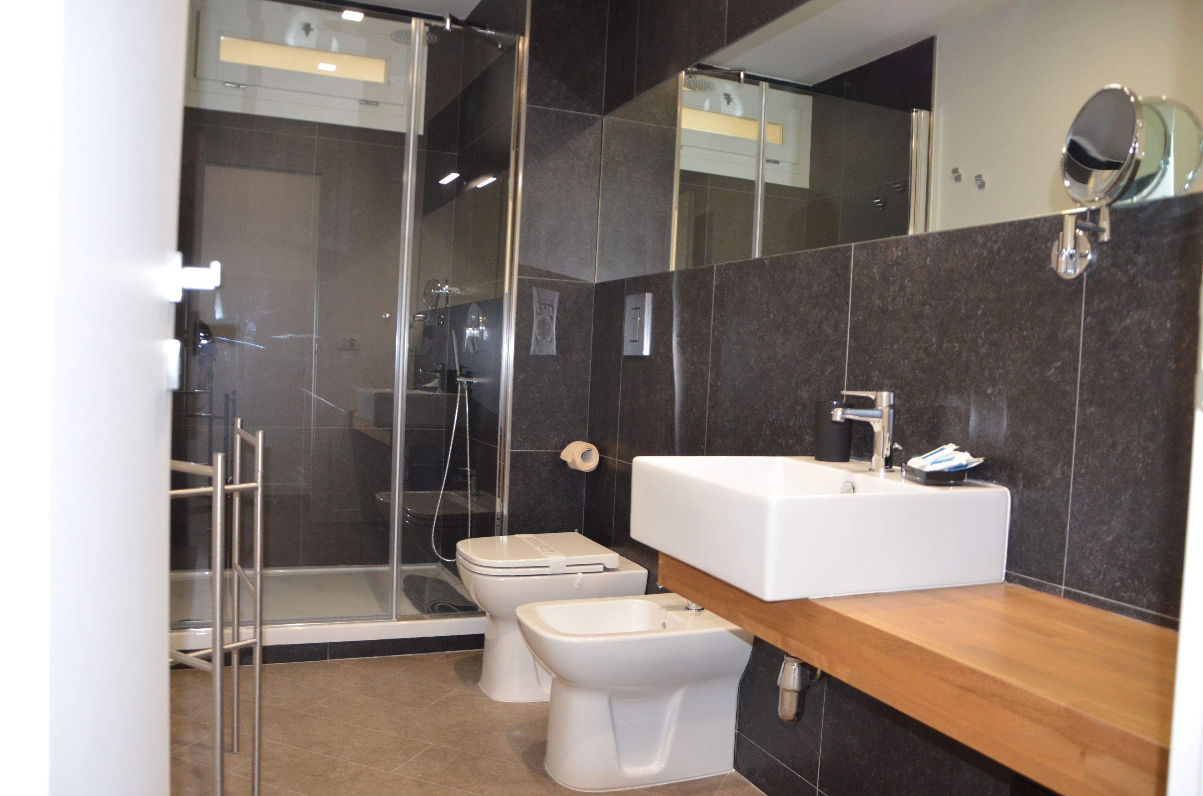 Een moderne badkamer met een douchecabine van glas, een witte wastafel en twee toiletten.