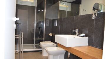 Een moderne badkamer met een douchecabine van glas, een witte wastafel en twee toiletten.