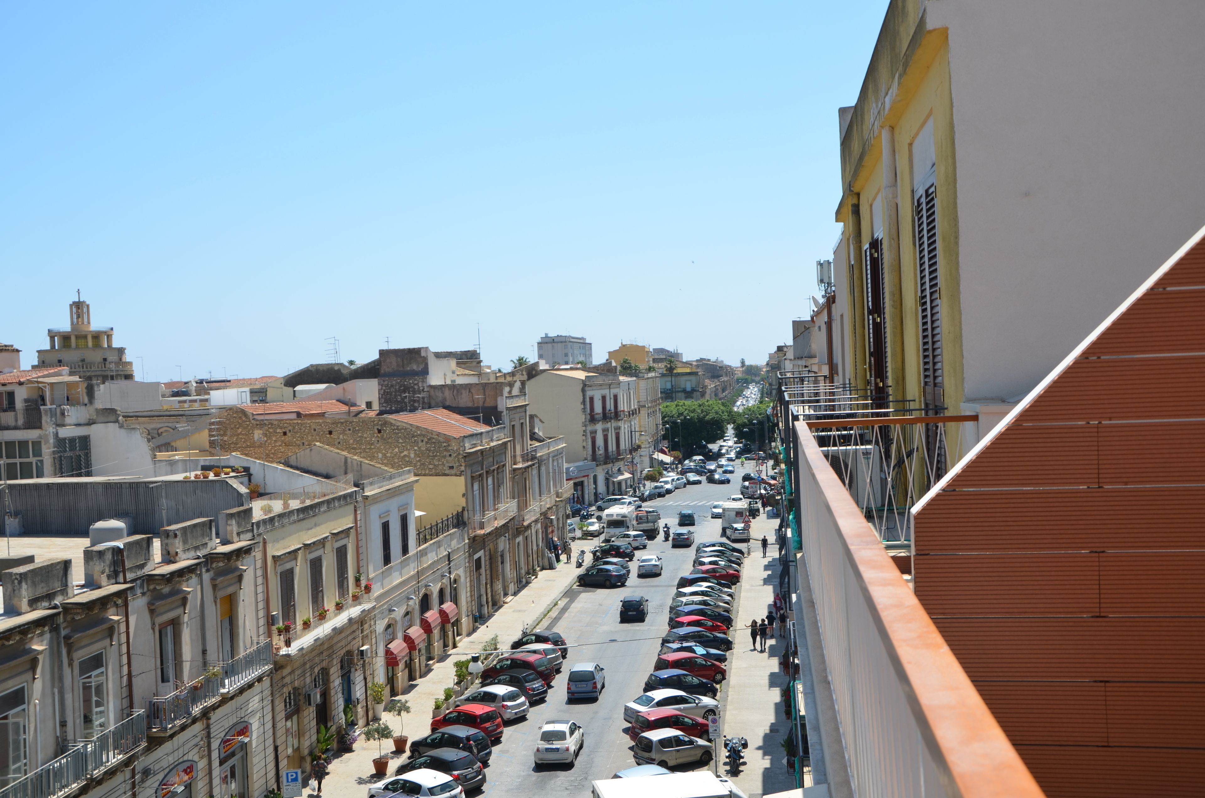 Vista de la calle con coches aparcados, edificios y cielo despejado.