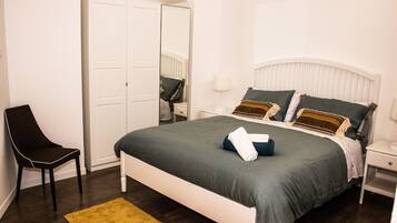 Ein Schlafzimmer mit Bett, Stuhl, Nachttisch, Lampe und einer Tür.