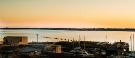 Une ville côtière avec des bâtiments et des bateaux, une jetée qui s’avance dans l’eau et un ciel au coucher du soleil.