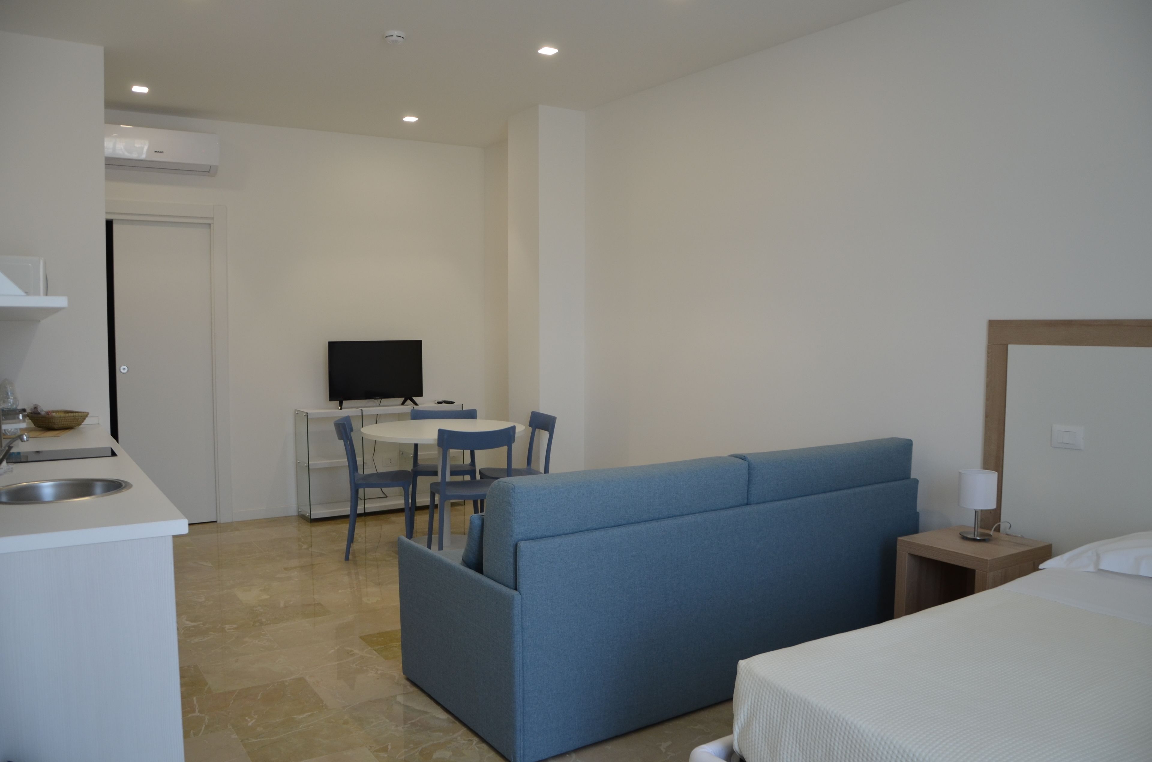 A compact hotel room with a kitchenette, a sofa, a bed, and a small table with chairs.
