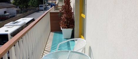 A balcony with a table and chairs, a potted plant, and a view of the street and buildings in the background.