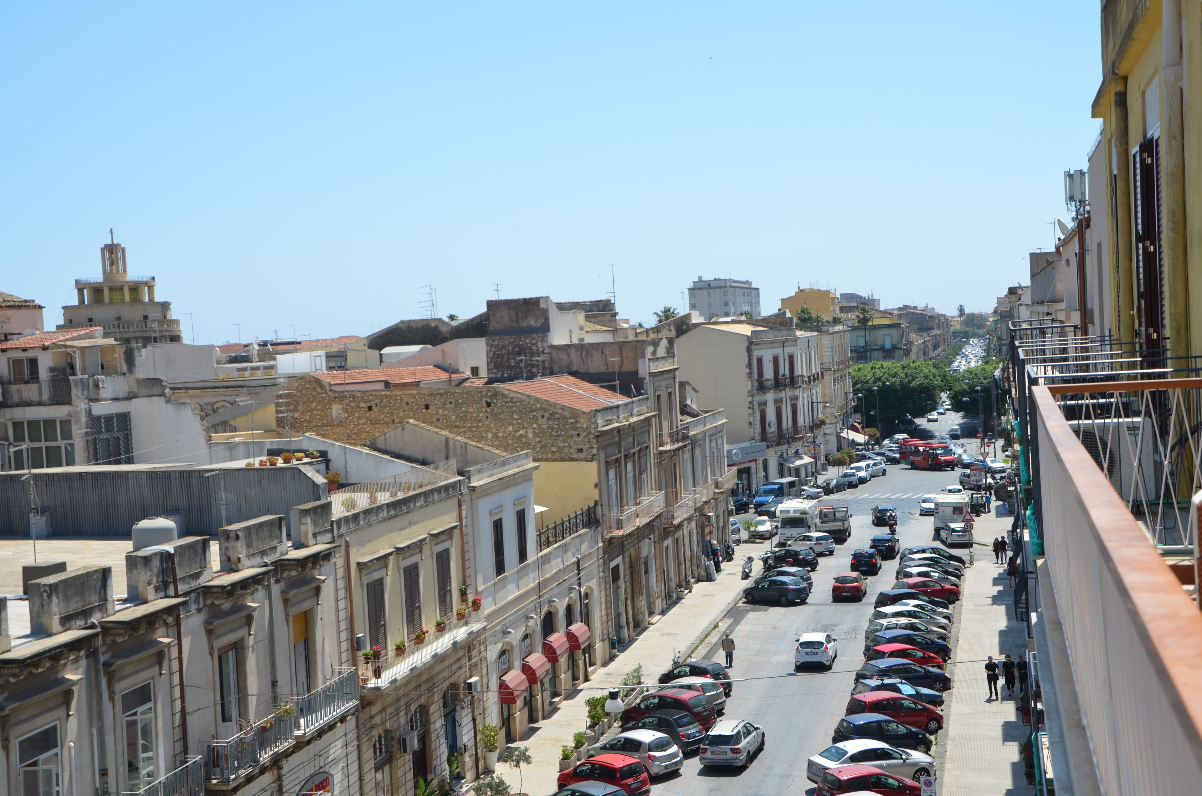Una calle estrecha bordeada de edificios históricos, coches aparcados y un cielo azul despejado.