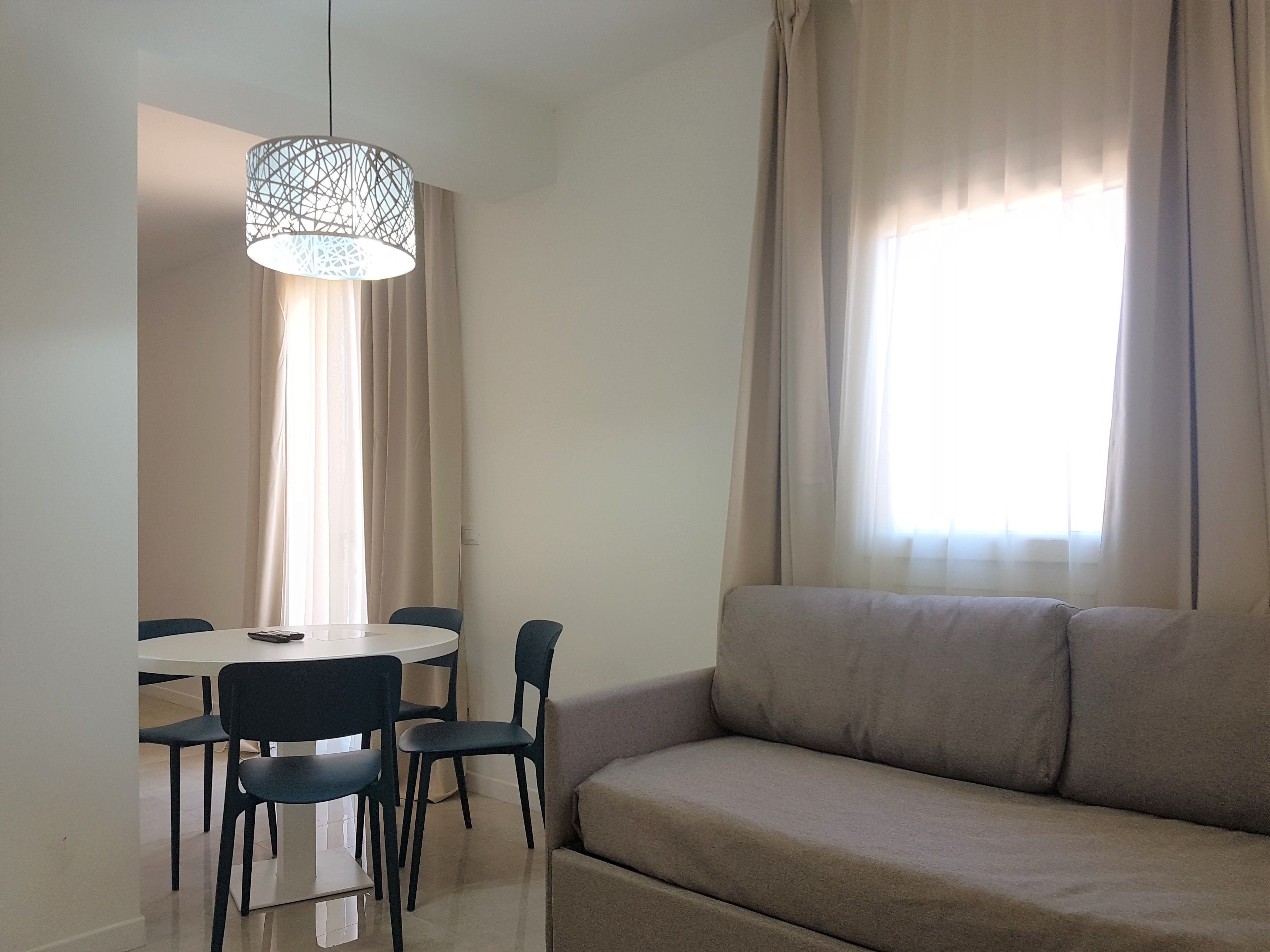 A modern living room with a beige sofa, a dining table with chairs, and a hanging light fixture.