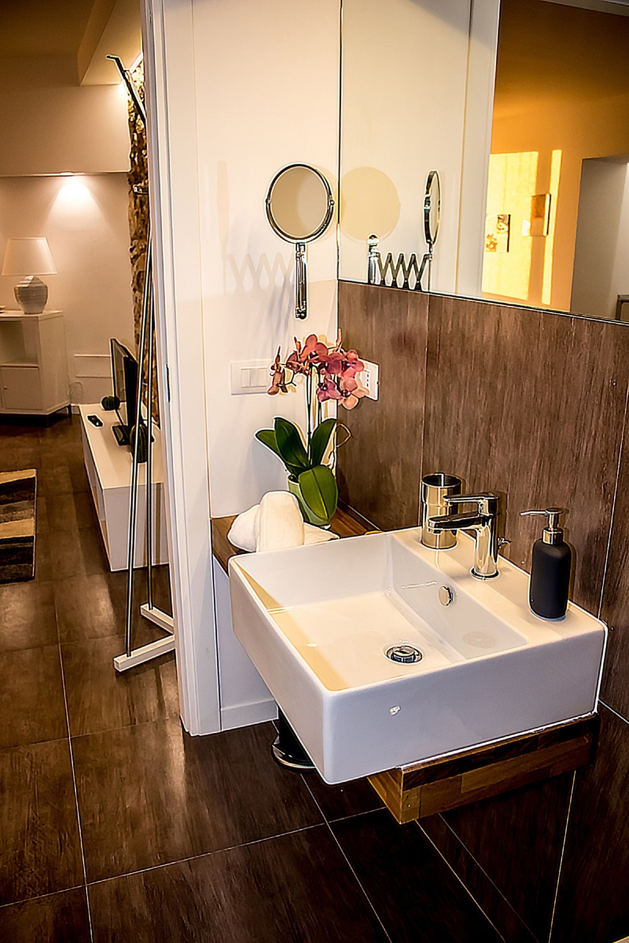 A modern bathroom with a large mirror, a white sink, and a wooden vanity.