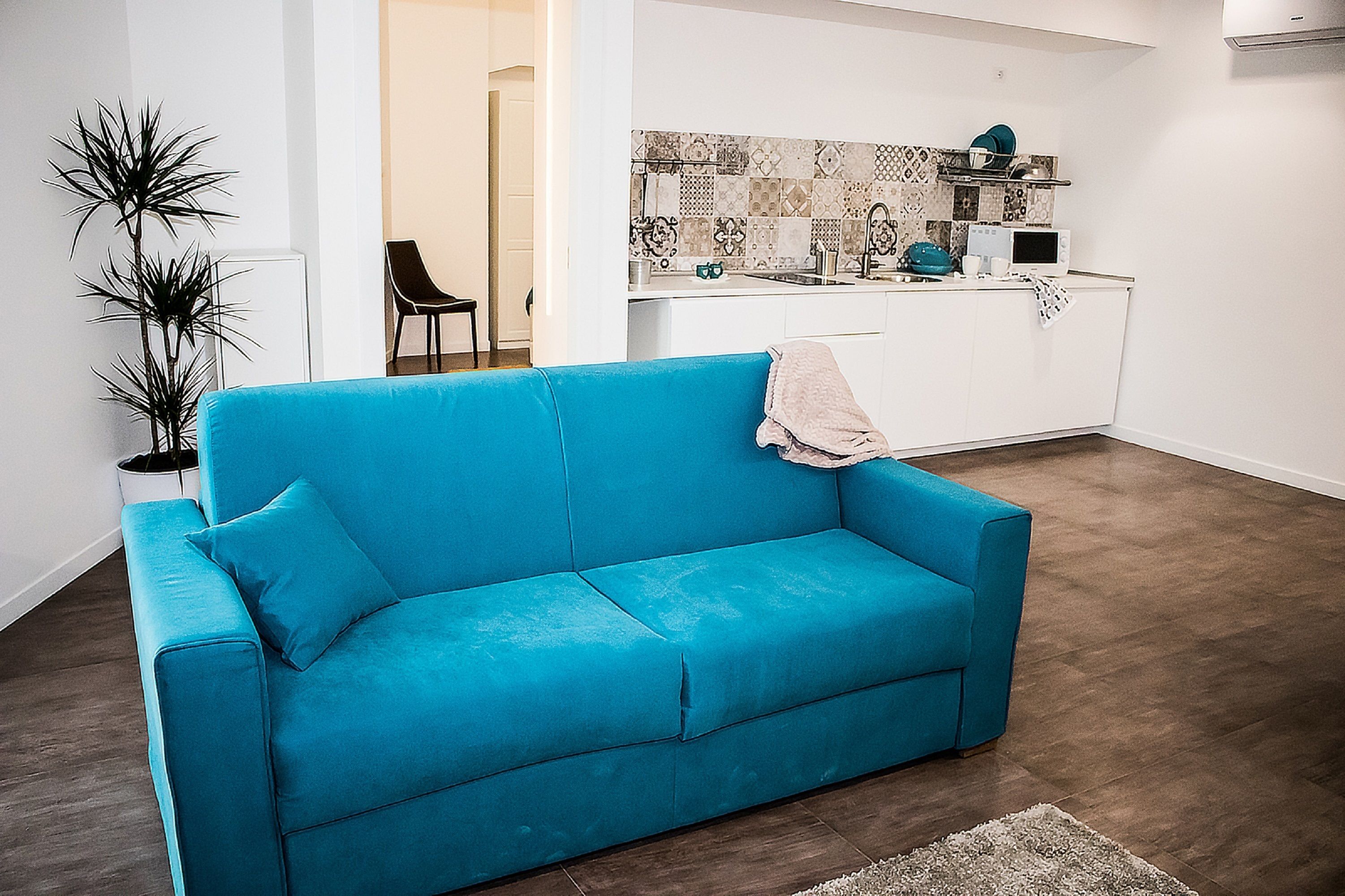 A bright blue sofa in a modern living room with a kitchen in the background.
