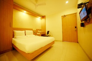 A hotel room with a large bed, wooden headboard, a flat-screen TV mounted on the wall, and a wooden door. - Horizon Heights Serviced Apartments (Coimbatore)