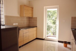 A kitchen with wooden cabinets, a black countertop, and a window with a view of greenery. - Horizon Heights Serviced Apartments (Coimbatore)