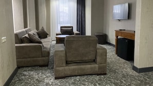 A hotel room with a sofa set, a small round table, a TV mounted on the wall, and a minibar. - Buyuk Kale Hotel (Kars)
