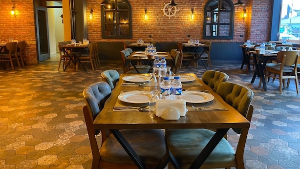 A restaurant with brick walls, hexagonal patterned flooring, and wooden tables set for dining. - Buyuk Kale Hotel (Kars)