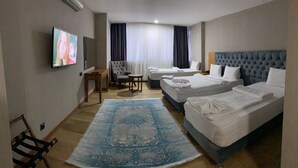 A hotel room with two single beds, a large flat-screen TV, a desk, a chair, and a blue patterned rug. - Buyuk Kale Hotel (Kars)