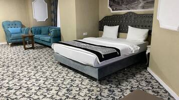 A hotel room with a large bed, a blue armchair, a small side table, and a patterned carpet.