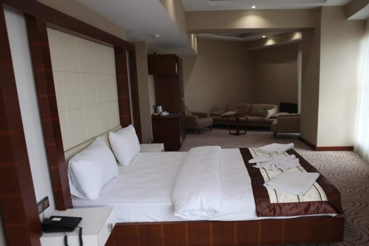 A hotel room with a large bed, a sofa, a TV, and a desk with a phone.