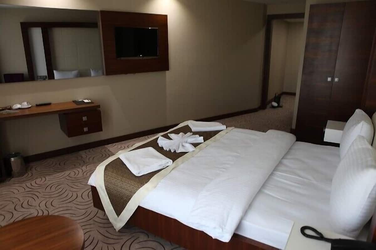 A hotel room with a neatly made bed, a wooden desk with a chair, a mirror, and a wardrobe.