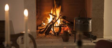 Een open haard met brandhout, een metalen pot en een kandelaar.