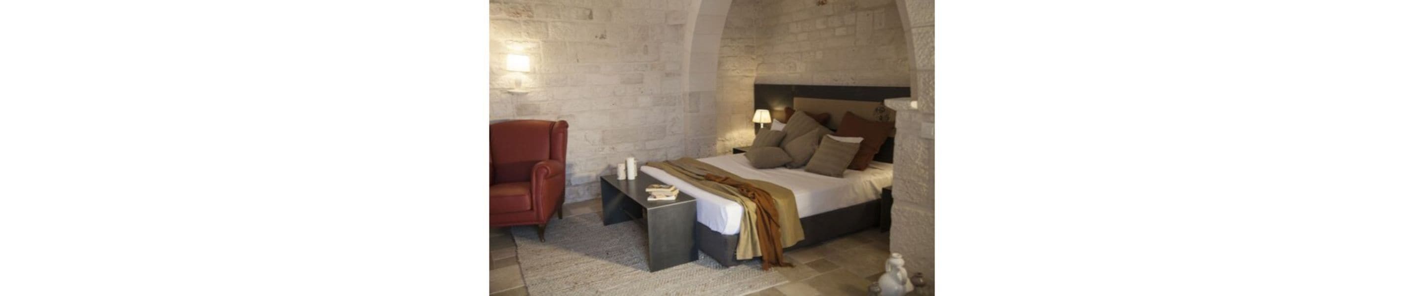 A bedroom with a bed, a chair, a nightstand, and a lamp.