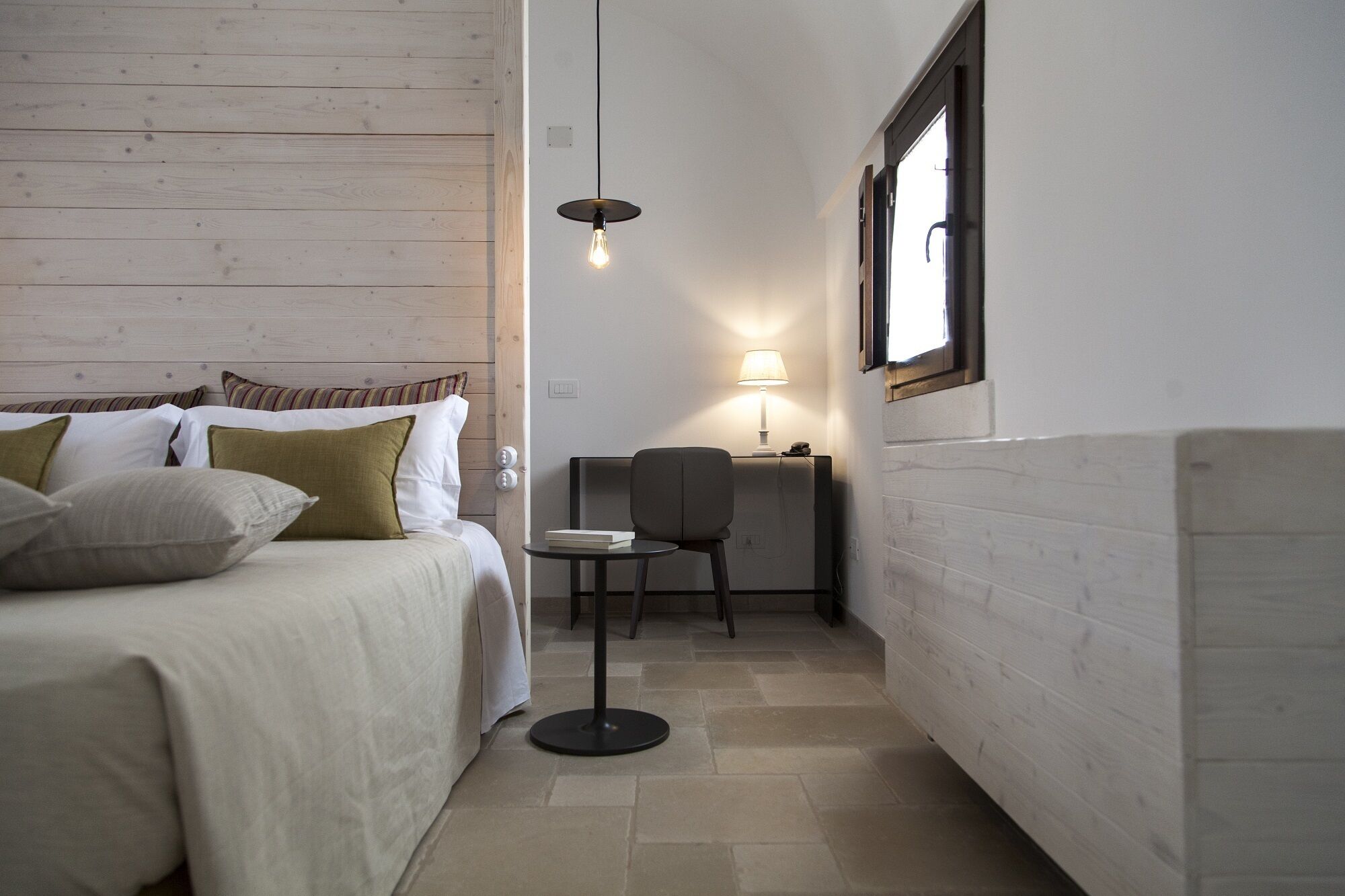 Ein kleines, ordentlich eingerichtetes Schlafzimmer mit Bett, Nachttisch, Stuhl und Lampe.