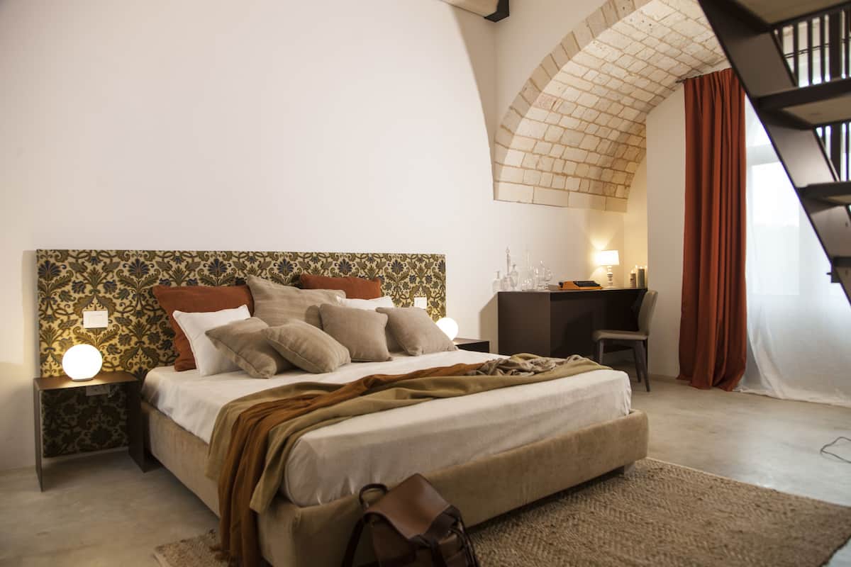 A bedroom with a large bed, a desk, and a staircase.