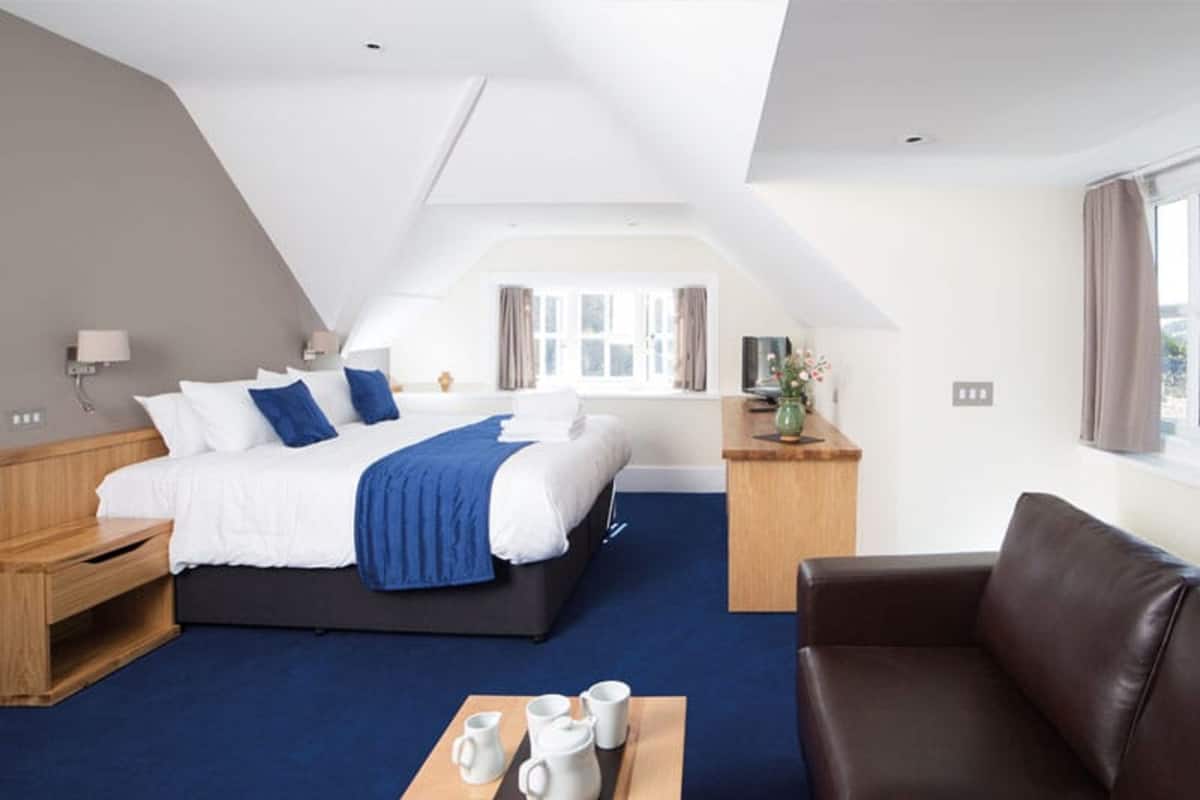 A modern hotel room with a large bed, a wooden nightstand, a leather sofa, and a dining table with tea set.