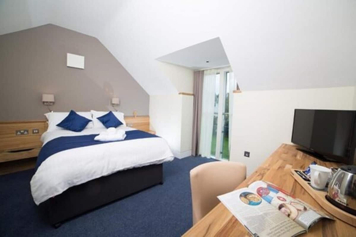 A modern hotel room with a bed, a desk, a television, and a magazine.