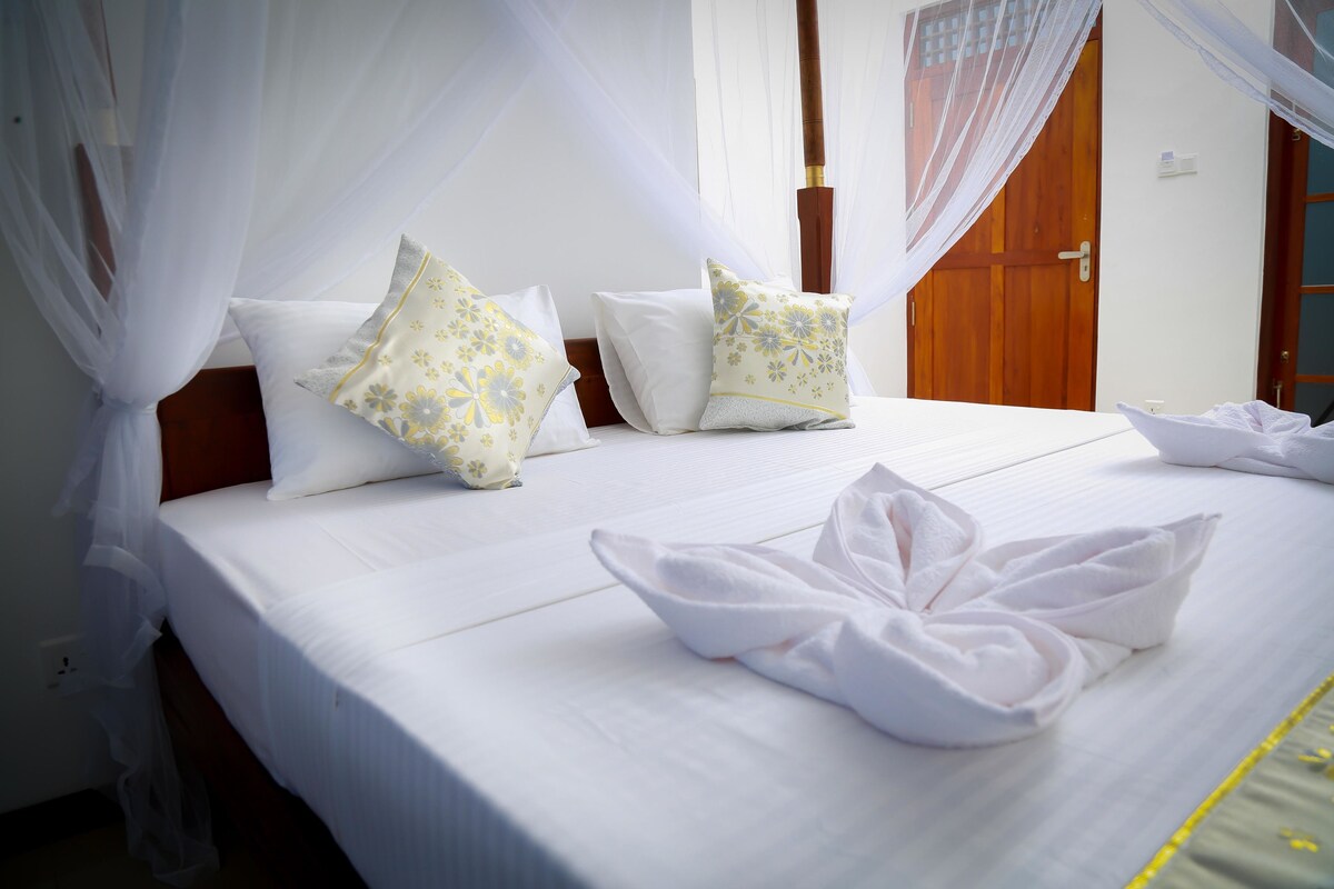 Uma cama bem arrumada com lençóis brancos, duas almofadas decorativas e uma toalha dobrada.