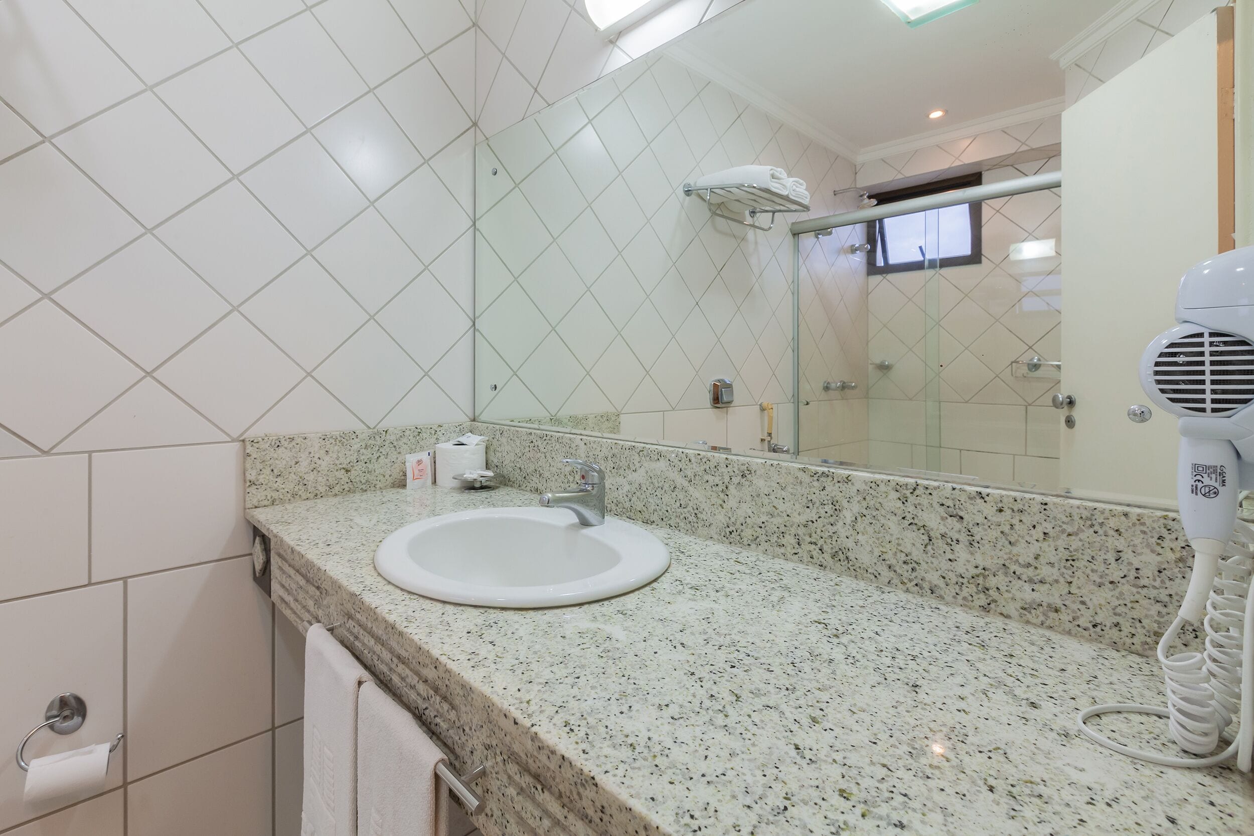 Baño con encimera de granito, lavamanos, espejo, toallero y secador de pelo.