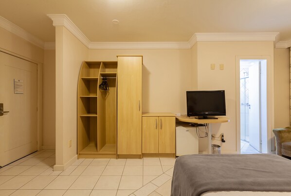 Una habitación de hotel con una cama, televisión, armario de madera y escritorio.