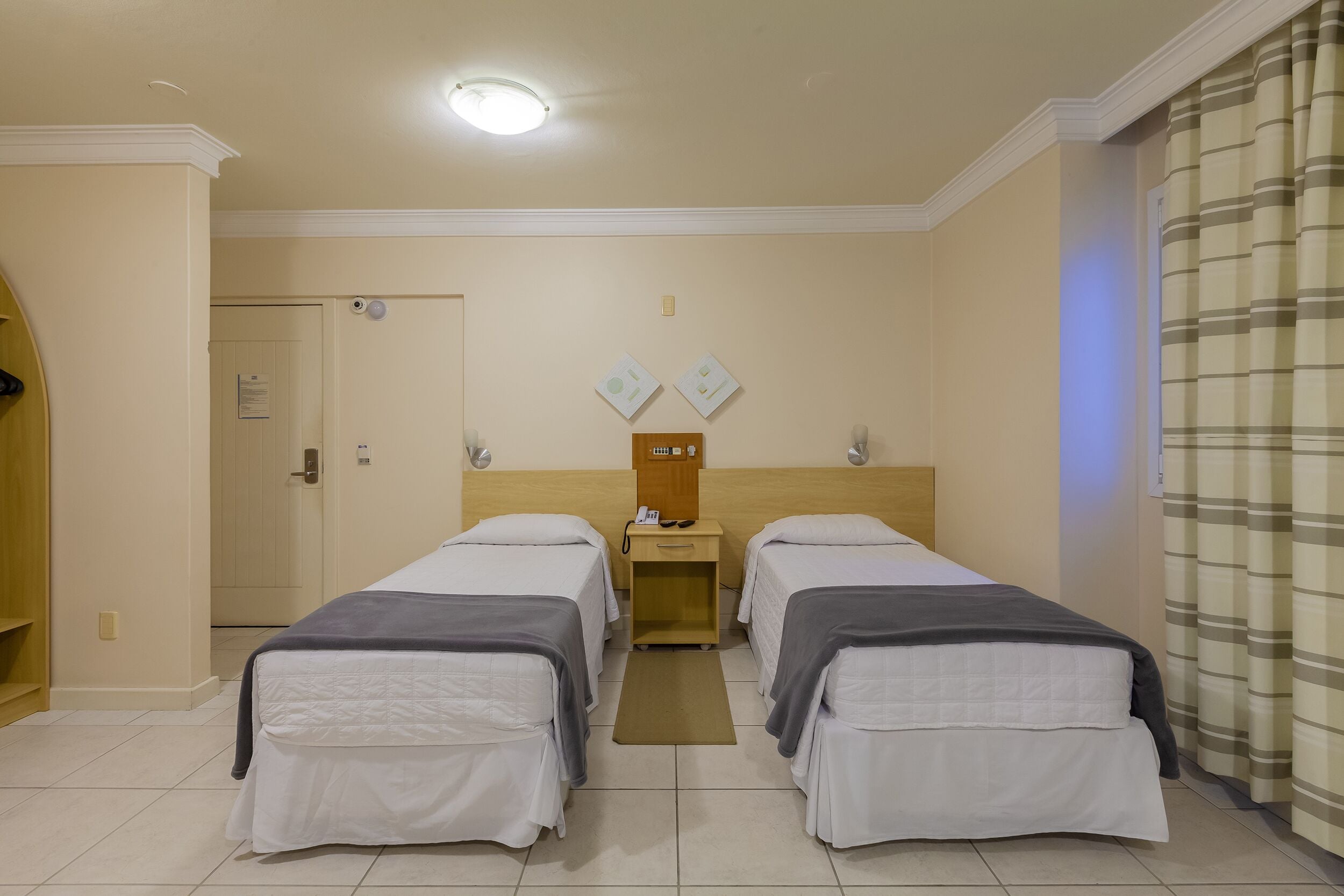 A hotel room with two beds, a nightstand, a mirror, and a door.