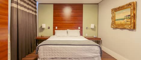 A hotel room with a large bed, wooden floor, a painting on the wall, and a checkered curtain.