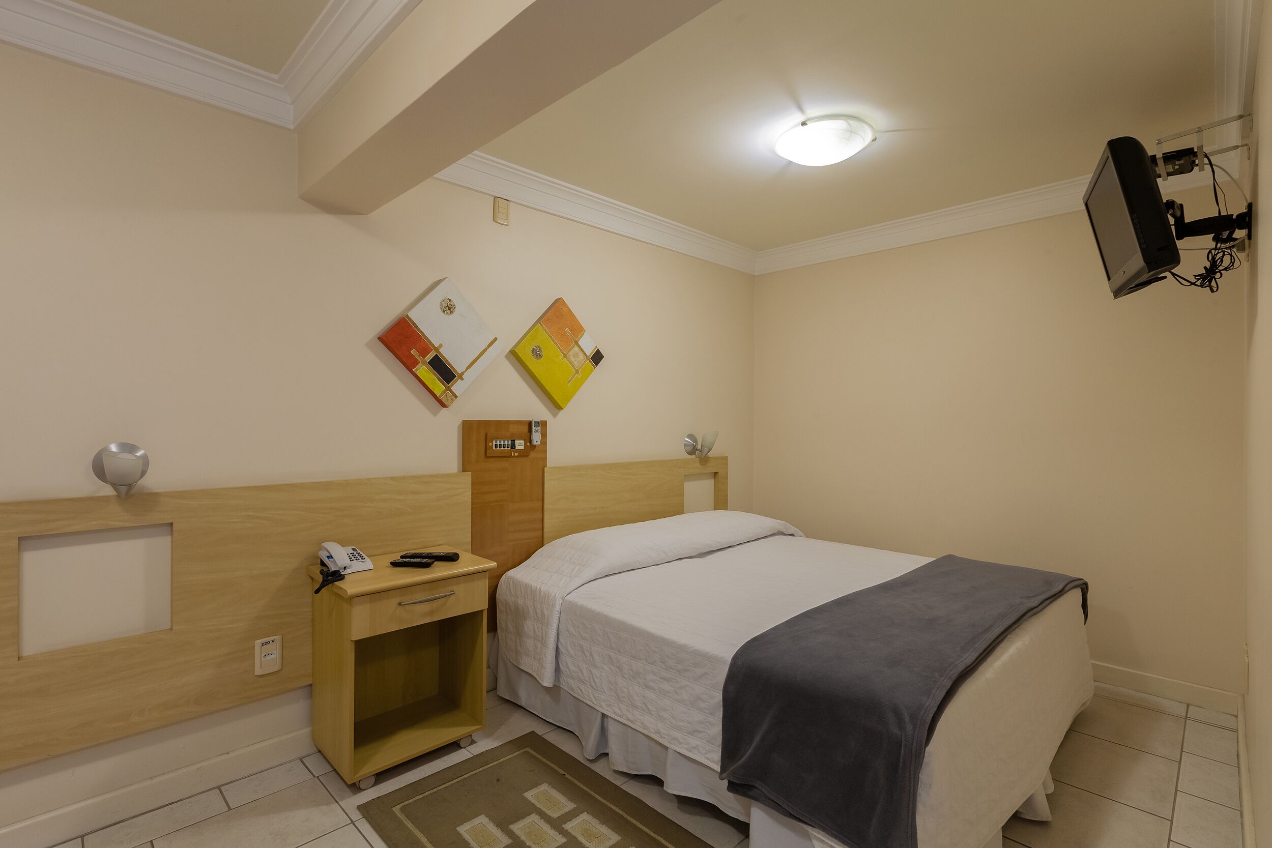 A hotel room with a bed, bedside table, and a small desk with a lamp.