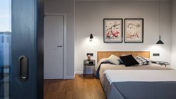 A modern bedroom with a large bed, wooden headboard, two framed artworks, bedside lamps, and a nightstand.