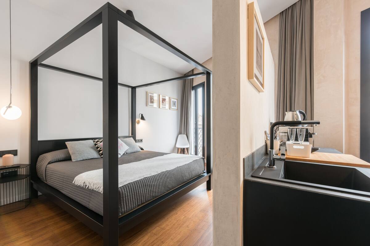 A modern room with a four-poster bed, a built-in sink, and a window with curtains.