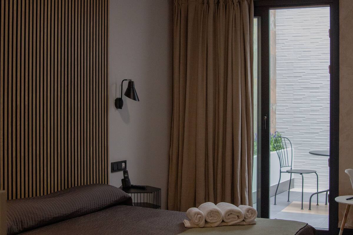 A modern hotel room with a bed, a desk, a chair, and a view of the outside.
