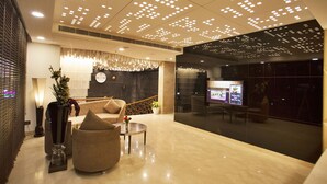 Een moderne lobby met een zithoek, een receptiebalie en een groot scherm met informatie.