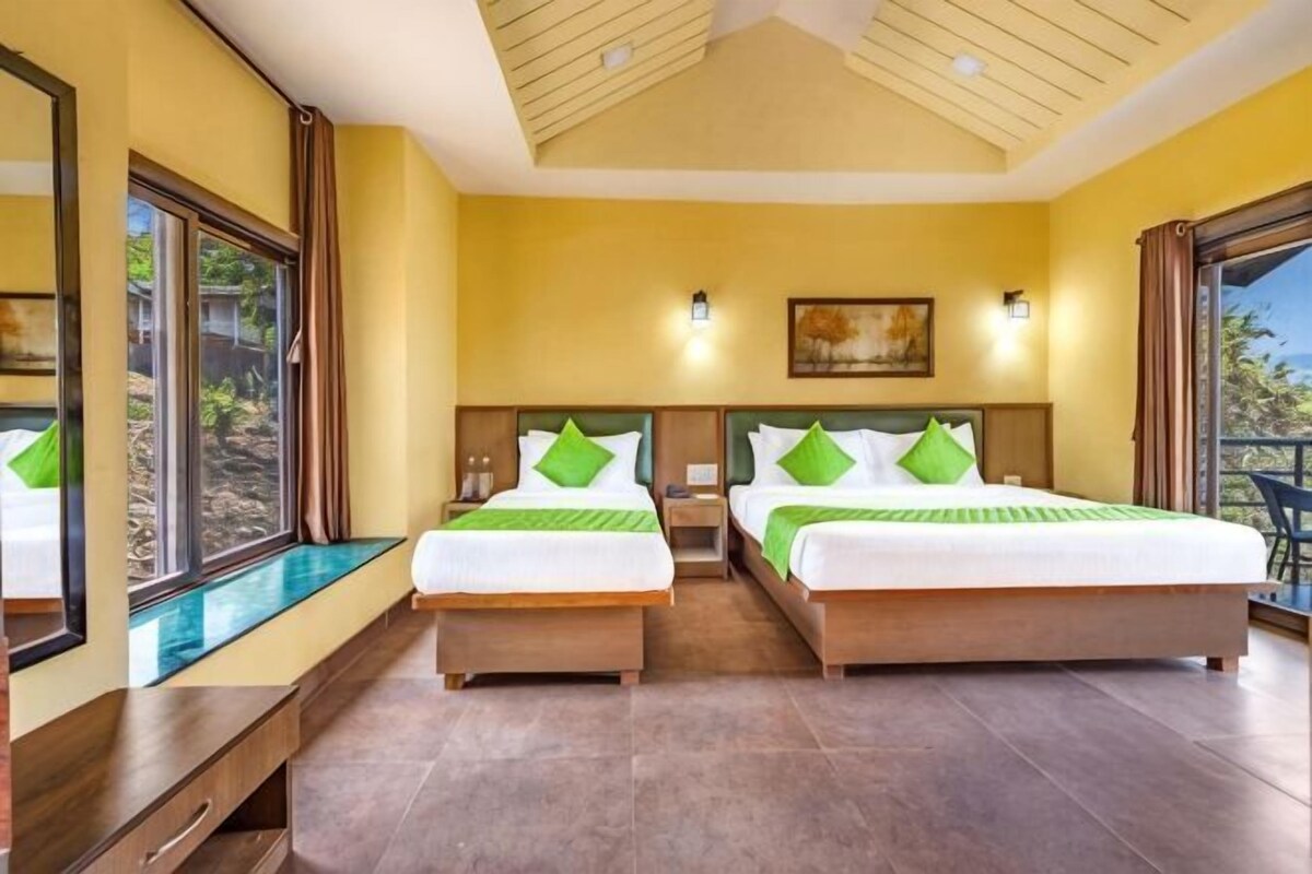 A hotel room with two beds, a large window, a ceiling fan, and a painting on the wall.