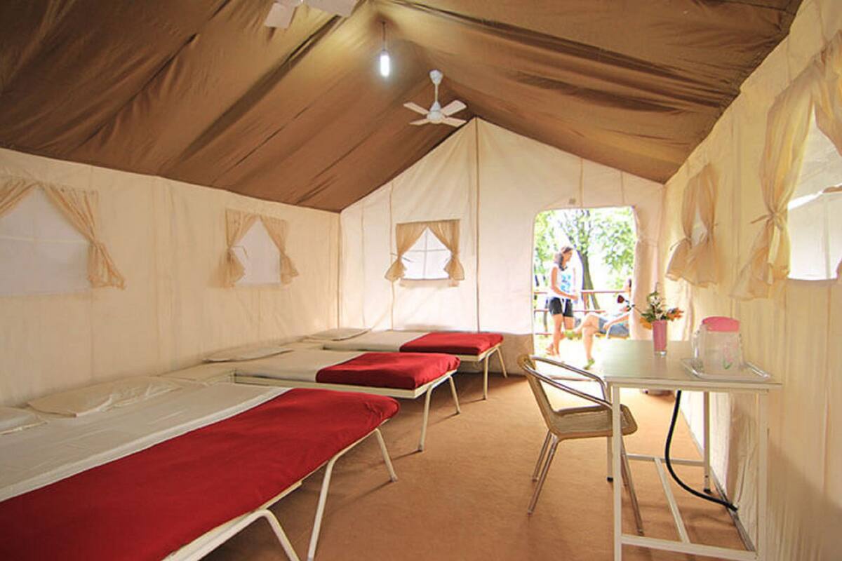A tented room with multiple beds, a table with a pink container, and a ceiling fan.