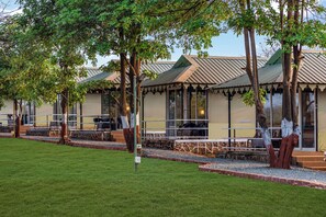 Una hilera de habitaciones de hotel con ventanales amplios, un área de estar al aire libre techada y un césped bien cuidado.
