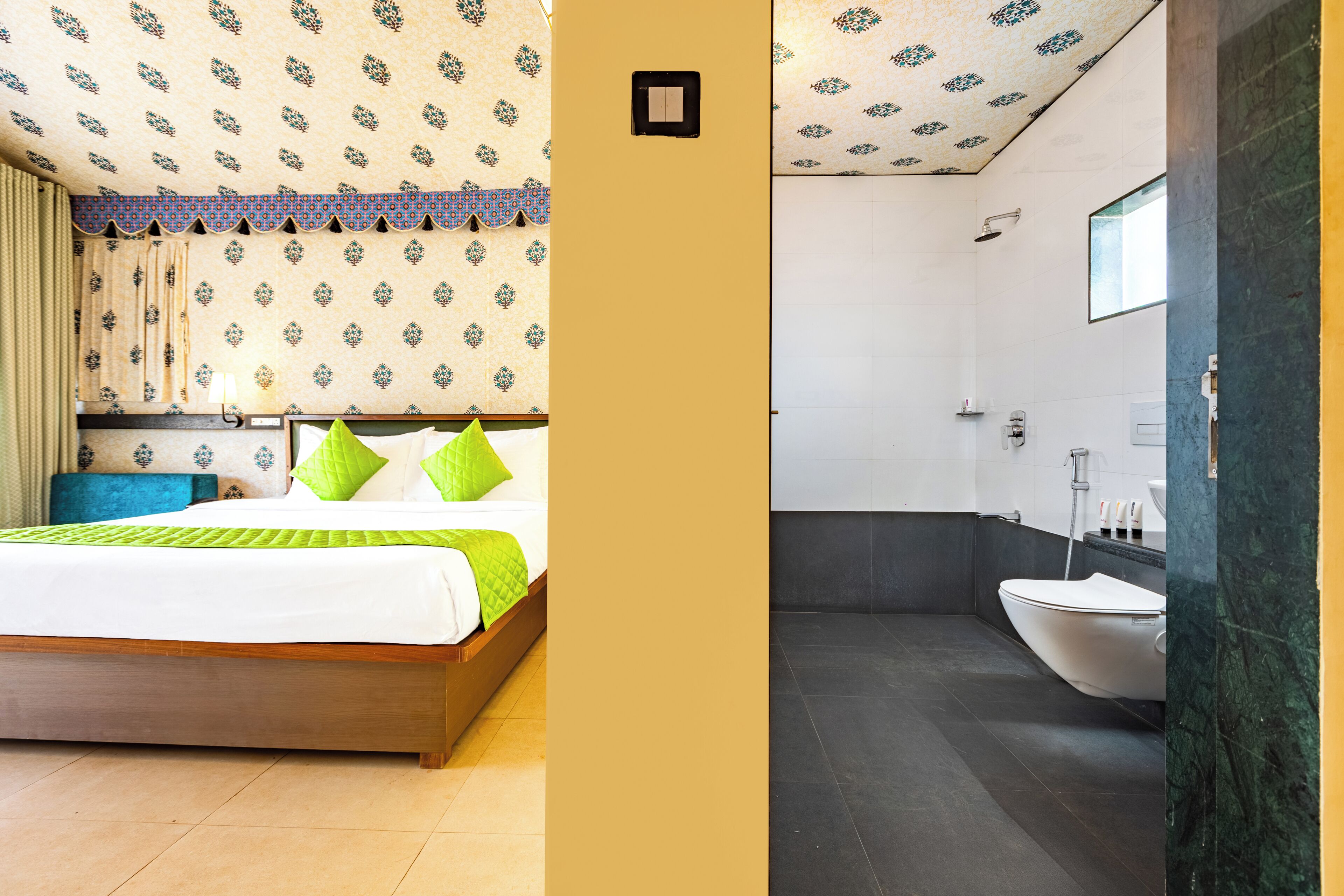 A hotel room with a bed, a bathroom with a sink and toilet, and patterned wallpaper.