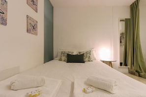 Una cama bien hecha con almohadas estampadas, una lámpara de noche y una cortina verde.
