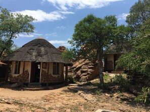 A thatched-roof building with stone wall decorations, surrounded by trees and rocky terrain. - Masama Lodge and Campsite (Serowe)