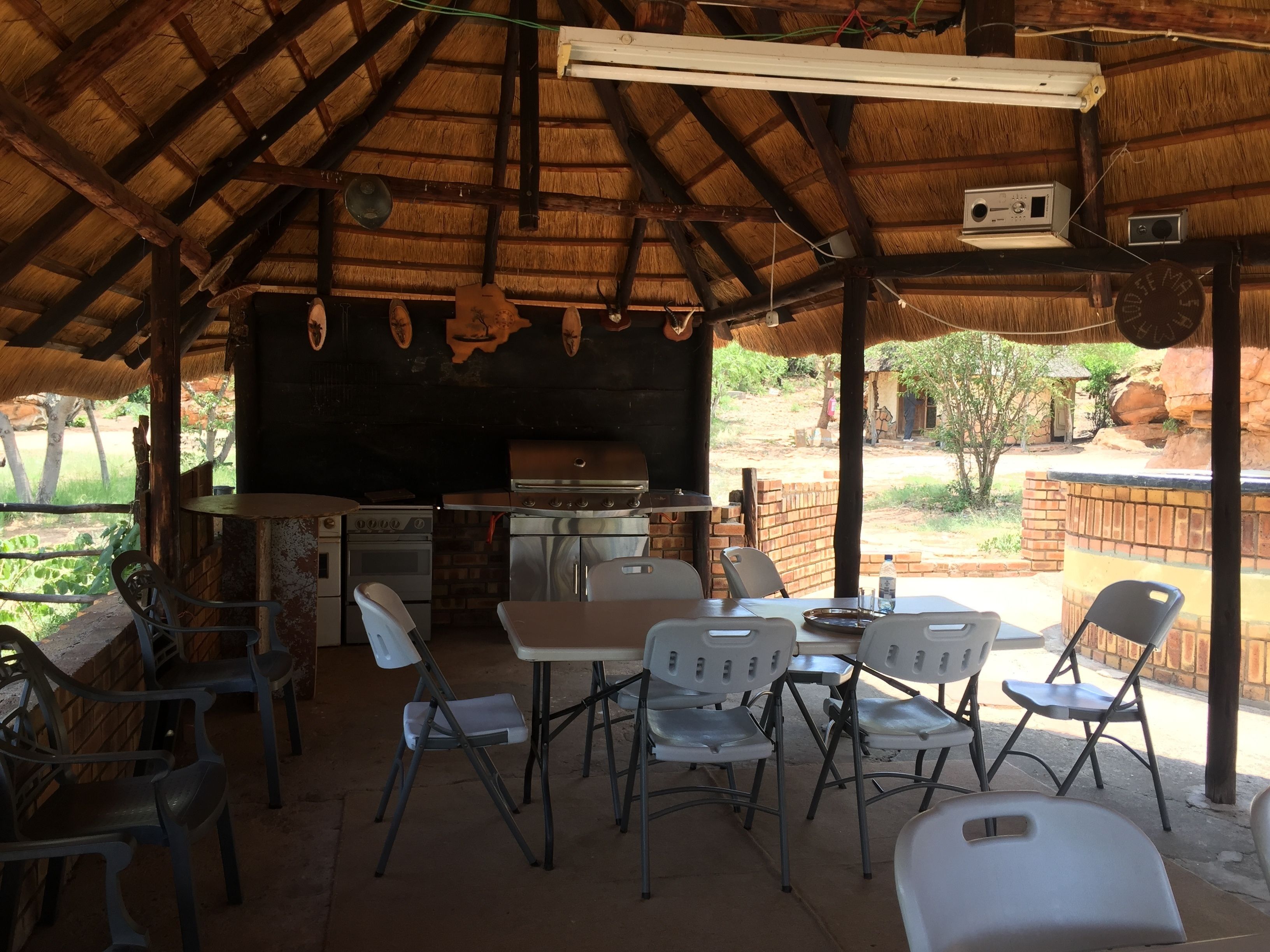 An outdoor dining area with a thatched roof, a grill, and a brick oven.