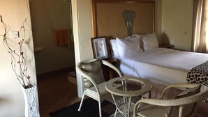 Habitación de hotel con cama, una silla, una mesita, un adorno en la pared y un techo de paja.