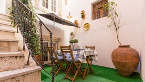 A small outdoor patio with a table and chairs, a large terracotta pot, and a staircase.