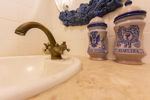 Un baño con un lavamanos blanco, un grifo de latón y dos recipientes de cerámica decorativos con diseños azules.