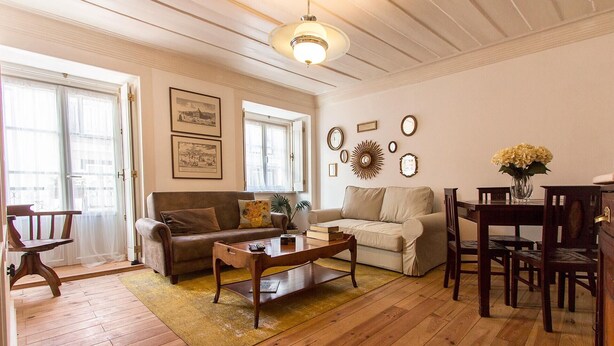 A living room with a wooden floor, a sofa, a coffee table, a dining table with chairs, and a chandelier.