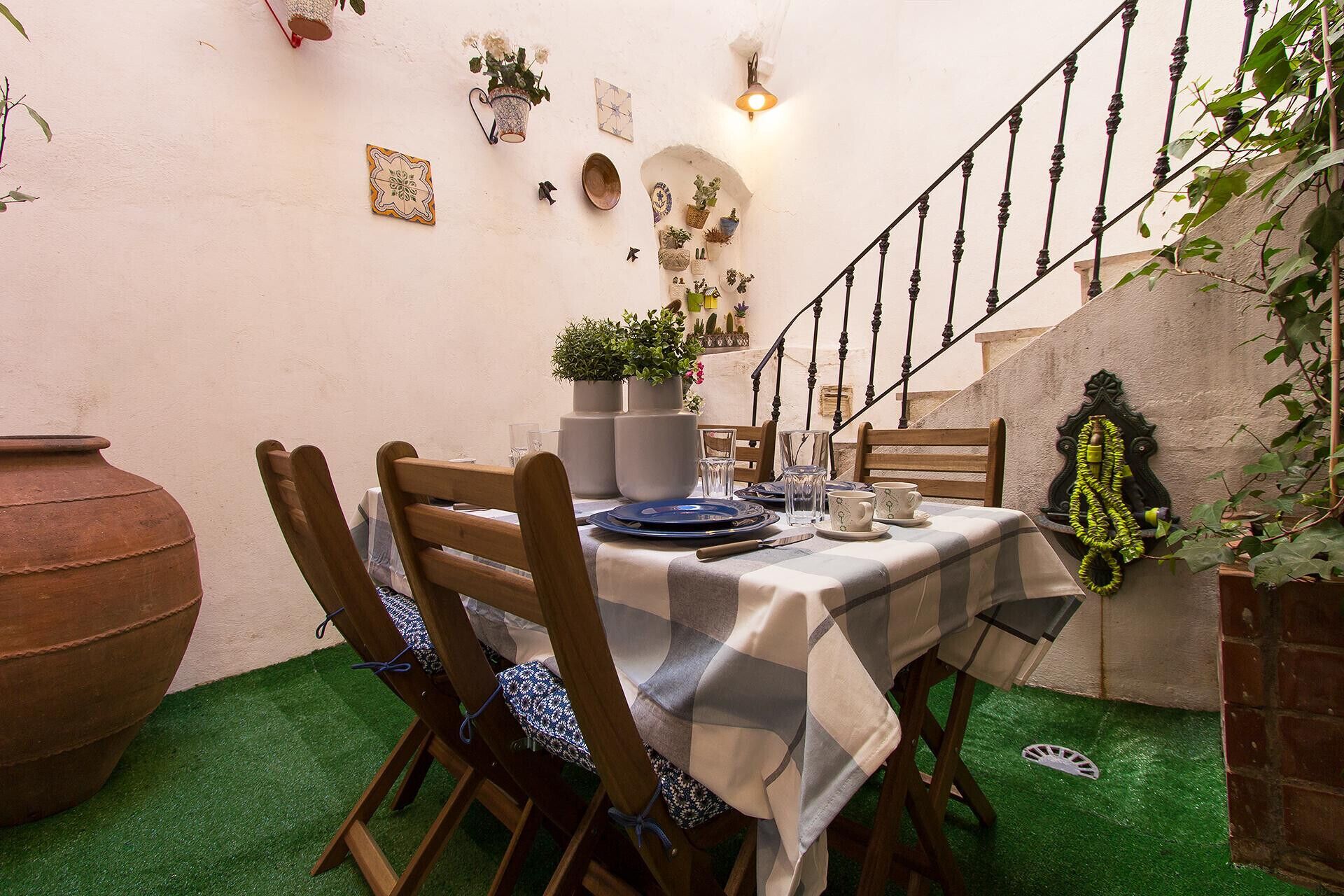 Een zithoek met een tafel gedekt voor twee personen, omringd door stoelen, een grote pot en diverse potplanten aan de wanden.