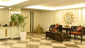 Zona de recepción con suelo a cuadros, un mostrador, dos sillas, una mesa de centro y plantas decorativas.