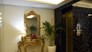 Un lobby lujoso con una consola dorada ornamentada, un espejo grande, una planta en maceta y un piso de mármol.