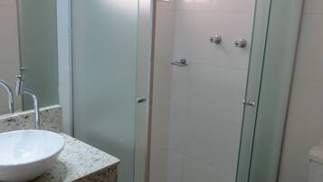 Un baño moderno con ducha envuelta en vidrio, lavamanos de granito y un inodoro con etiqueta de marca visible.